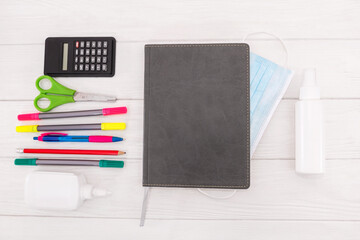 notebook, pen, school supplies and mask on a white wooden background.