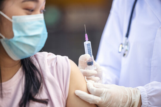 Female Doctor Holding Syringe Making Covid 19 Vaccination Injection Dose In Shoulder Of Female Patient Wearing Mask. Flu Influenza Vaccine Clinical Trials Concept, Corona Virus Treatment