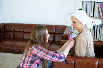 Caucasian daughter Put on a Awareness pink ribbon on Elderly mother shirt in white headscarf. Pink ribbon common cancer is symbol of various campaign activities for patients with breast cancer. - Powered by Adobe
