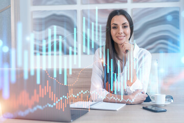 Attractive businesswoman in white shirt at workplace working with laptop to optimize trading strategy at corporate finance fund. Forex chart hologram over office background