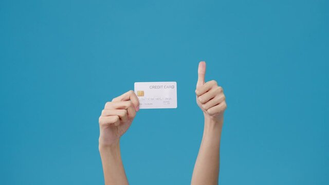 Young girl hold in hand credit bank card showing thumb up isolated over blue background in studio. Copy space for place a text, message for advertisement. Advertising area, mockup promotional content.