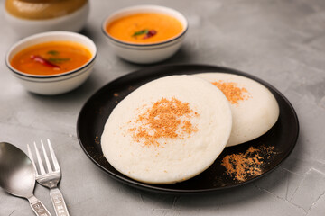 Thatte idli or Plate idly with sambar coconut chutney, chutney podi popular breakfast of Kerala South India Sri Lanka. Healthy steamed rice cakes steaming fermented batter black lentils and rice.