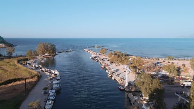 Coastal drone top view of moored boats on sheltered harbor with green plantation. Aerial shot of caiques, fishing and modern small ships at Georgioupoli, Greece in Crete island with calm waters.