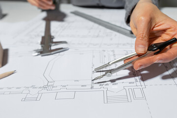 The architect measures with a dividers for drawing on paper. The designer draws a sketch of the room.