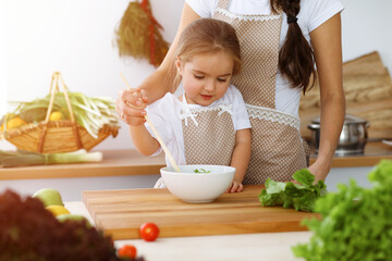 Happy woman and her daughter making healthy vegan salad and snacks for family feasting in sunny kitchen. Christmas, New year, Thanksgiving, Anniversary, Mothers Day. Healthy meal cooking concept