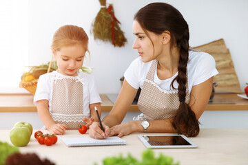 Happy woman and her daughter are searching for new recipes for a family feasting, sunny kitchen. Christmas, New year, Thanksgiving, Anniversary, Mothers Day. Healthy meal cooking concept