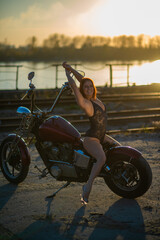 Red-haired woman in sexy lingerie in high heels sits on a motorcycle. Attractive red-haired girl sits on a motorcycle at sunset