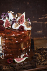 Caramel cake with wild berries, cream and figs on brown background