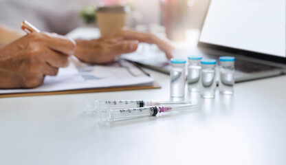 Focus on the syringe on table and blurred hand of doctor working with laptop and searching data of corona virus