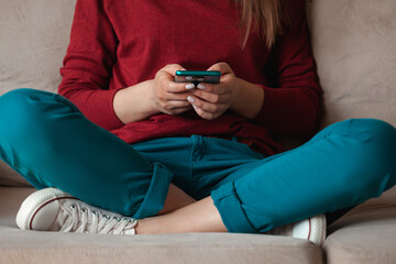 Woman using mobile phone, holding in hands sitting on sofa
