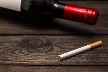 Bottle of red wine and cigarette lying on an old wooden table. Close up view, focus on the cigarette