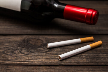 Bottle of red wine and two cigarettes lying on an old wooden table. Close up view, focus on the cigarette