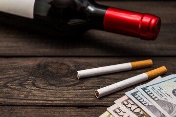 Bottle of red wine and two cigarettes with money on an old wooden table. Close up view, focus on the cigarette
