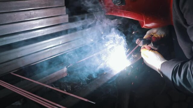 Manufacturing process, welding work, welding of metal parts with a soldering iron, a professional in protective uniform in a closed heavy industry factory. Installation of metal structures