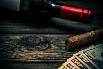 Bottle of red wine and cuban cigar with money on an old wooden table. Close up view, focus on the...
