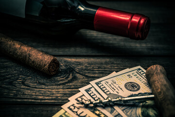 Bottle of red wine and cuban cigar with money and corkscrew on an old wooden table. Close up view,...