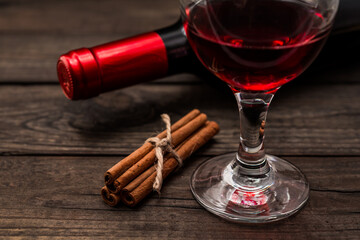 Bottle of red wine with a glass of red wine and  cinnamon sticks tied with jute rope on an old wooden table. Close up view, focus on the cinnamon sticks