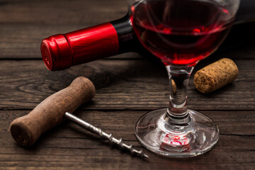 Bottle of red wine with a glass of red wine and cork on an old wooden table. Close up view