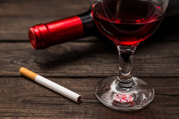 Bottle of red wine with a glass of red wine and cigarette on an old wooden table. Close up view, focus on the cigarette
