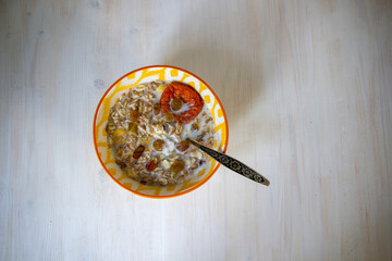 Yellow bowl with muesli, milk, raisins, dried apricots, spoon on white background
