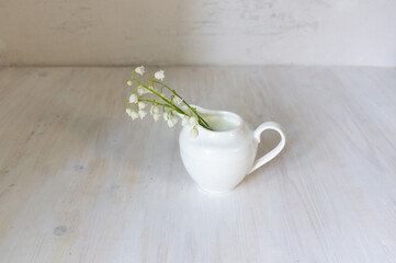 Milk jug with lily of the valey flowers on white background