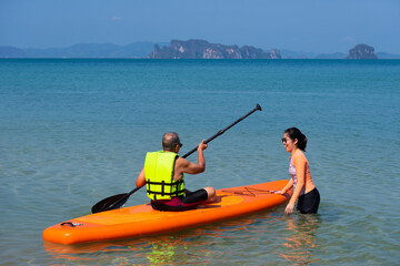 asian senior father playing standing up paddleboard or SUP with young daughter at blue sea on summer vacation. family together concept