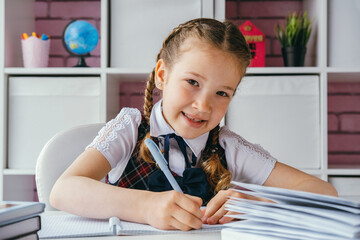 Portrait beautiful positive little schoolgirl sitting at her desk and doing her homework. Back to school concept.