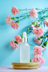 Naklejka na ściany i meble Blank transparent beauty serum dropperon a blue background with blooming pink carnation flowers. Beauty care concept advertisment poster.