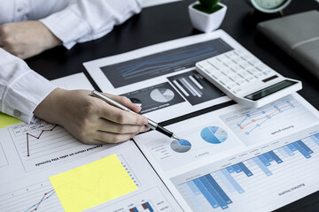A close-up businesswoman holding a pen and pointing at a company financial statement, she is checking monthly financial documents from the finance department. The financial concept of the company.