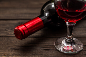 Bottle of red wine with a glass of red wine on an old wooden table. Close up view, focus on the bottle of red wine