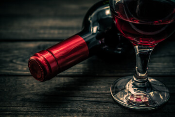 Bottle of red wine with a glass of red wine on an old wooden table. Close up view, focus on the bottle of red wine