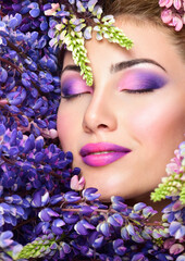 Beautiful woman face surrounded by violet flowers. Spring Flower. Springtime. Professional makeup,
