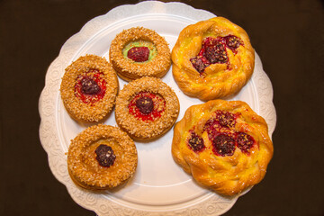 Naklejka na ściany i meble Pastry made of puff pastry in the form of round twisted buns with jam and coconut shavings on an openwork white napkin of a round shape. Confectionery products for tea and coffee.