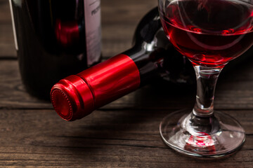 Two bottles of red wine with a glass of red wine on an old wooden table. Close up view, focus on the bottle of red wine