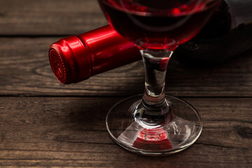 Bottle of red wine with a glass of red wine on an old wooden table. Close up view, focus on the glass of red wine