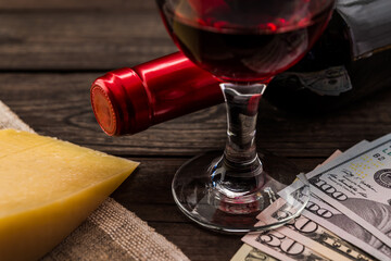 Bottle of red wine with a glass of red wine and a piece of parmesan with money on an old wooden table. Close up view, focus on the glass of red wine