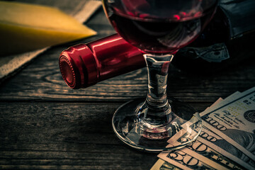 Bottle of red wine with a glass of red wine and a piece of parmesan with money on an old wooden table. Close up view, focus on the glass of red wine