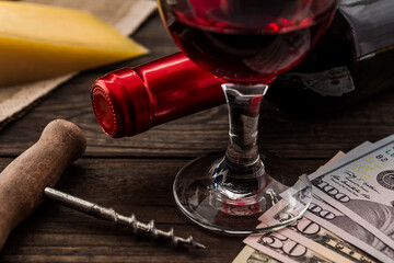 Bottle of red wine with a glass of red wine and a piece of parmesan with money on an old wooden table. Close up view, focus on the glass of red wine
