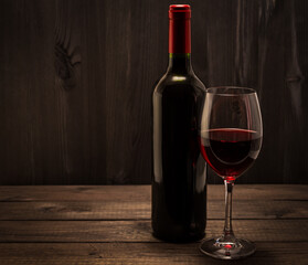 Bottle of red wine with a glass of red wine on an old wooden table