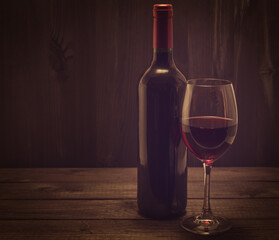 Bottle of red wine with a glass of red wine on an old wooden table