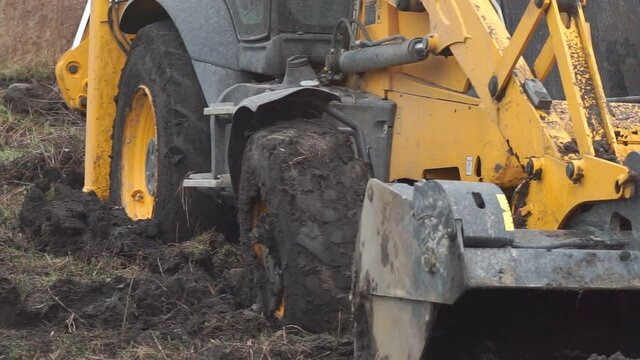 The big tractor wheel is stuck in the mud. Yellow tractor wheel on a farm field stuck in chernozem and about to hit the road