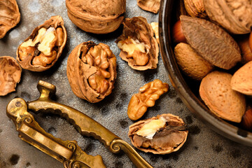 Almonds, walnuts and hazelnuts are sitting in a brown bowl and a nutcracker on a dark brown spotted plate.