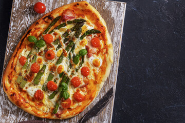 Pizza with bacon, eggs and asparagus top view on dark with copy space