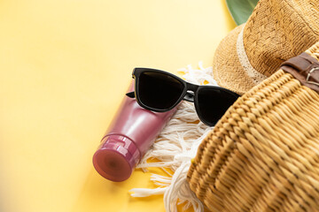 Sun glasses, sunscreen cream and straw beach bag on yellow background. Summer vacation concept