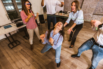 Group having fun together with limbo game at office party. - obrazy, fototapety, plakaty