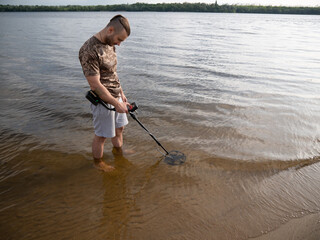 Guy in the river is looking for treasure with a metal detector in the water.