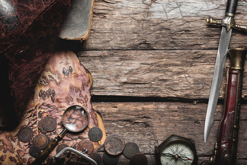 Old treasure map, coins, compass, weapon and pirate hat on the old wooden table flat lay background...