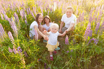 Happy family mother father embracing kids outdoor. Woman man baby child and teenage girl sitting on summer field with blooming flowers background. Happy family mom dad and daughters playing on meadow.