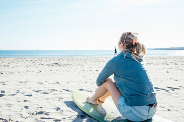 Young girl sitting on surfboard on the beach. Summer concept.