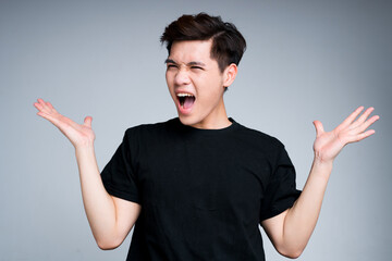 Cheerful Asian guy screaming with happiness raising his hands and dancing. Isolated on gray background.